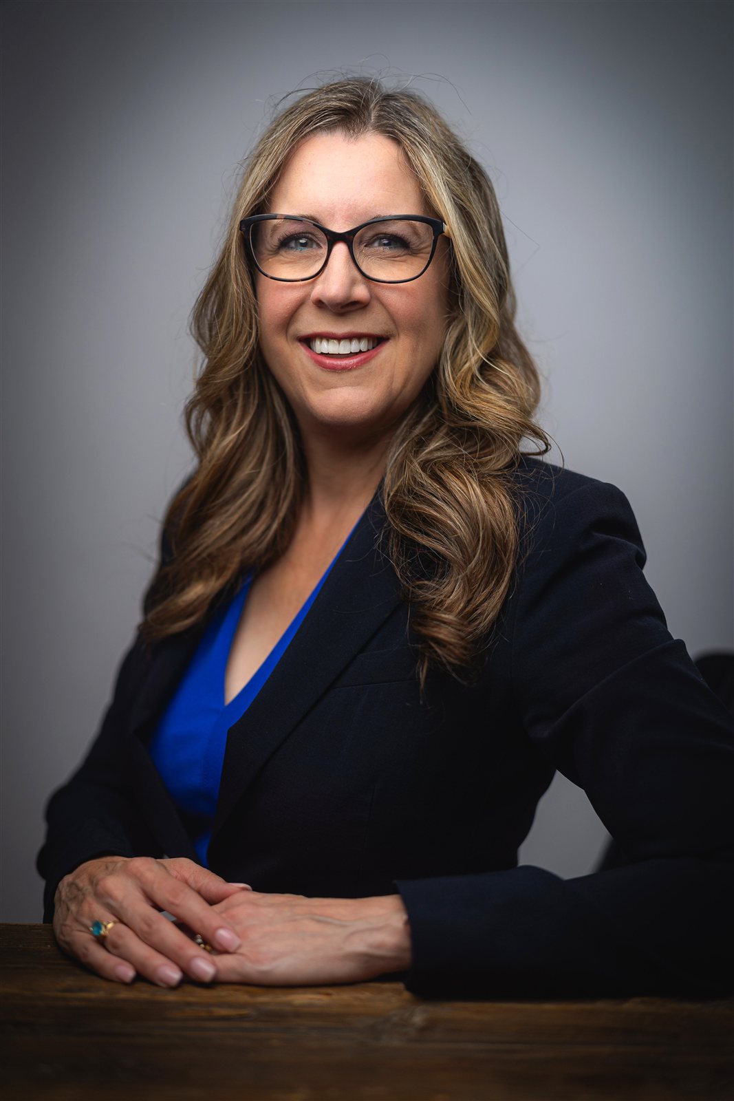 Jennifer Davis seated at a table, smiling at the camera in a navy blazer